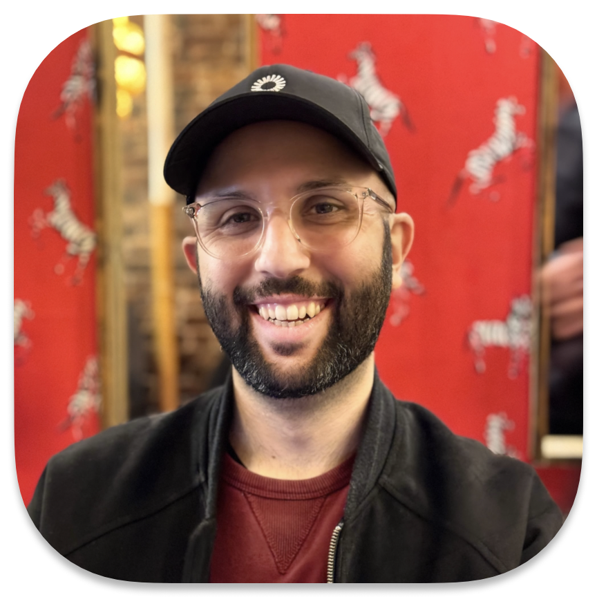 portrait photo of me, a smiling bearded white man in a red sweater, a black bomber jacket, and a black baseball cap